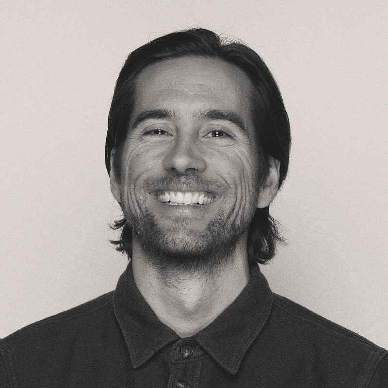 Smiling dark-haired man with a short beard wearing a dark collared shirt in a grayscale portrait.